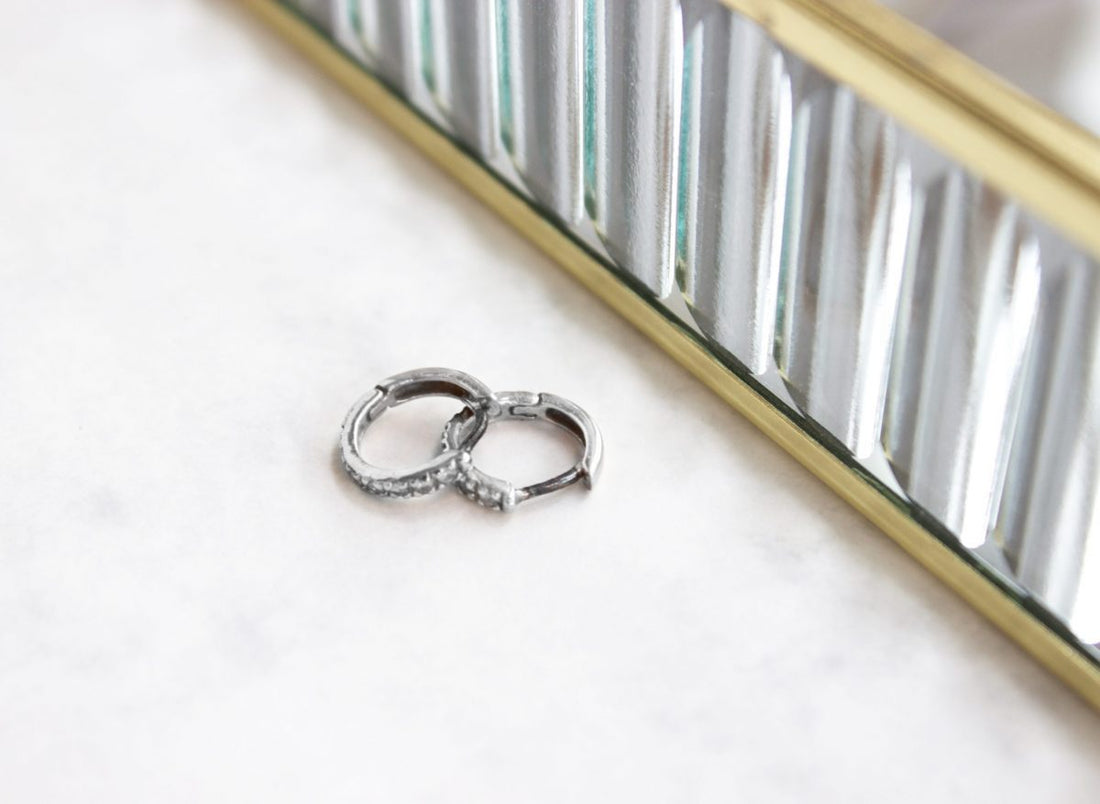 Two tarnished sterling silver huggie hoop earrings on a marble surface